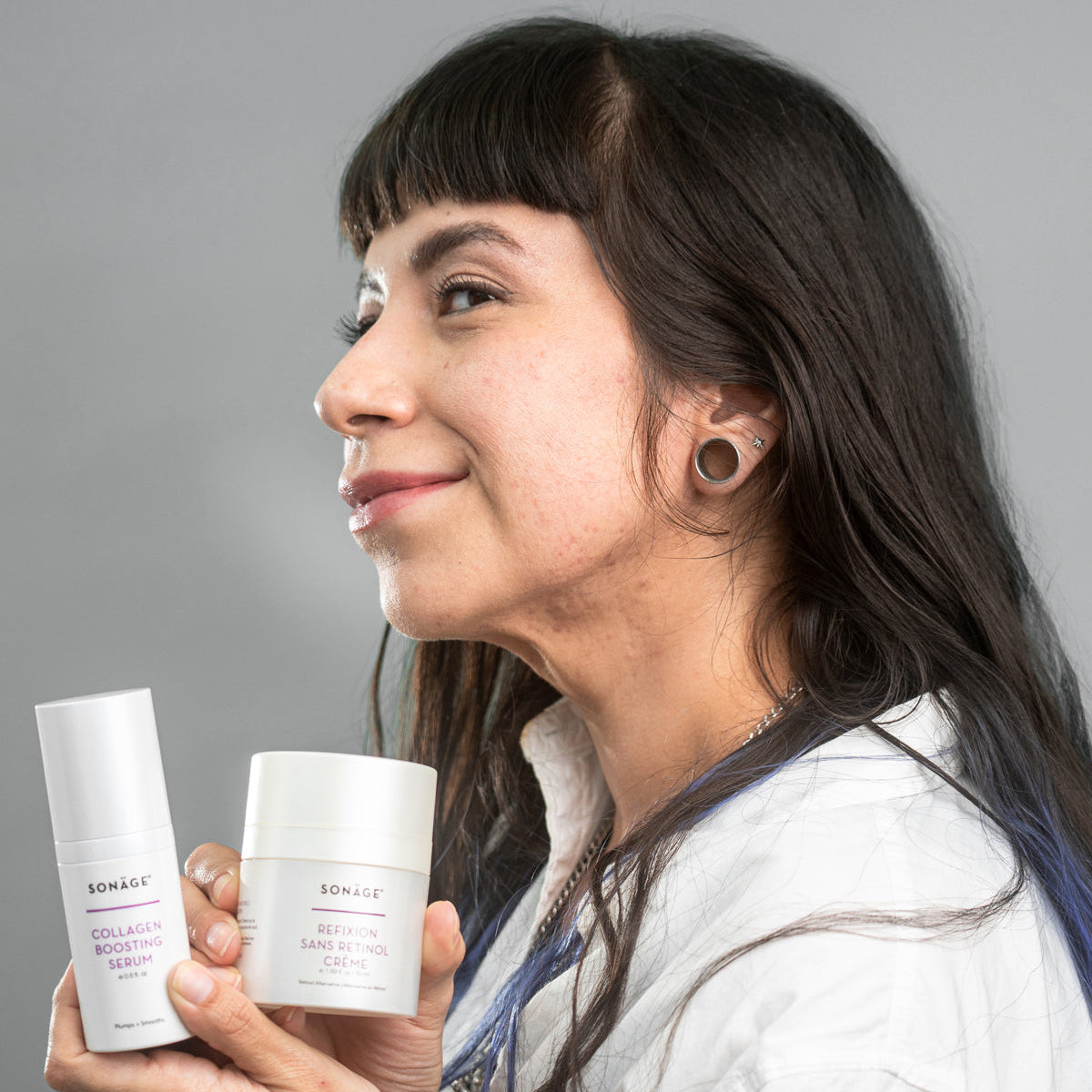 Woman holding two skincare products against a gray background