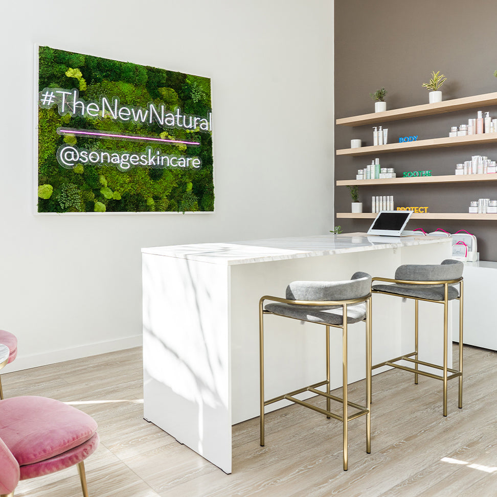 Modern interior with a reception desk, stools, and shelves displaying products with a '#TheNewNatural @sonageskincares' sign.