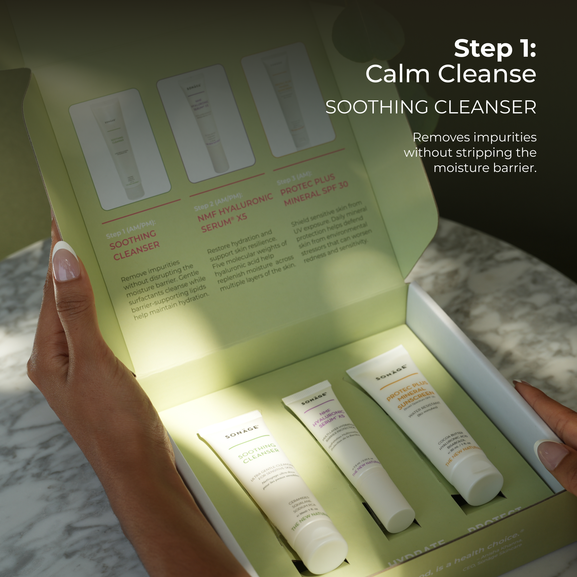 Opened Sensitive Skin Barrier Recovery Kit box on a marble circular table with its sides being held by two hands revealing the inside design of the box and three white tube Sonage skincare products