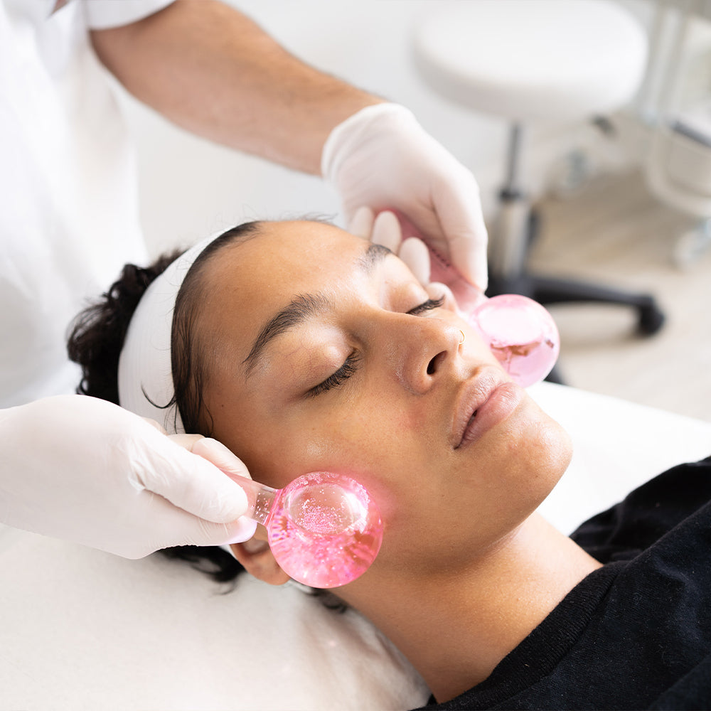 Person receiving a facial treatment with pink icy globes in a clinical setting