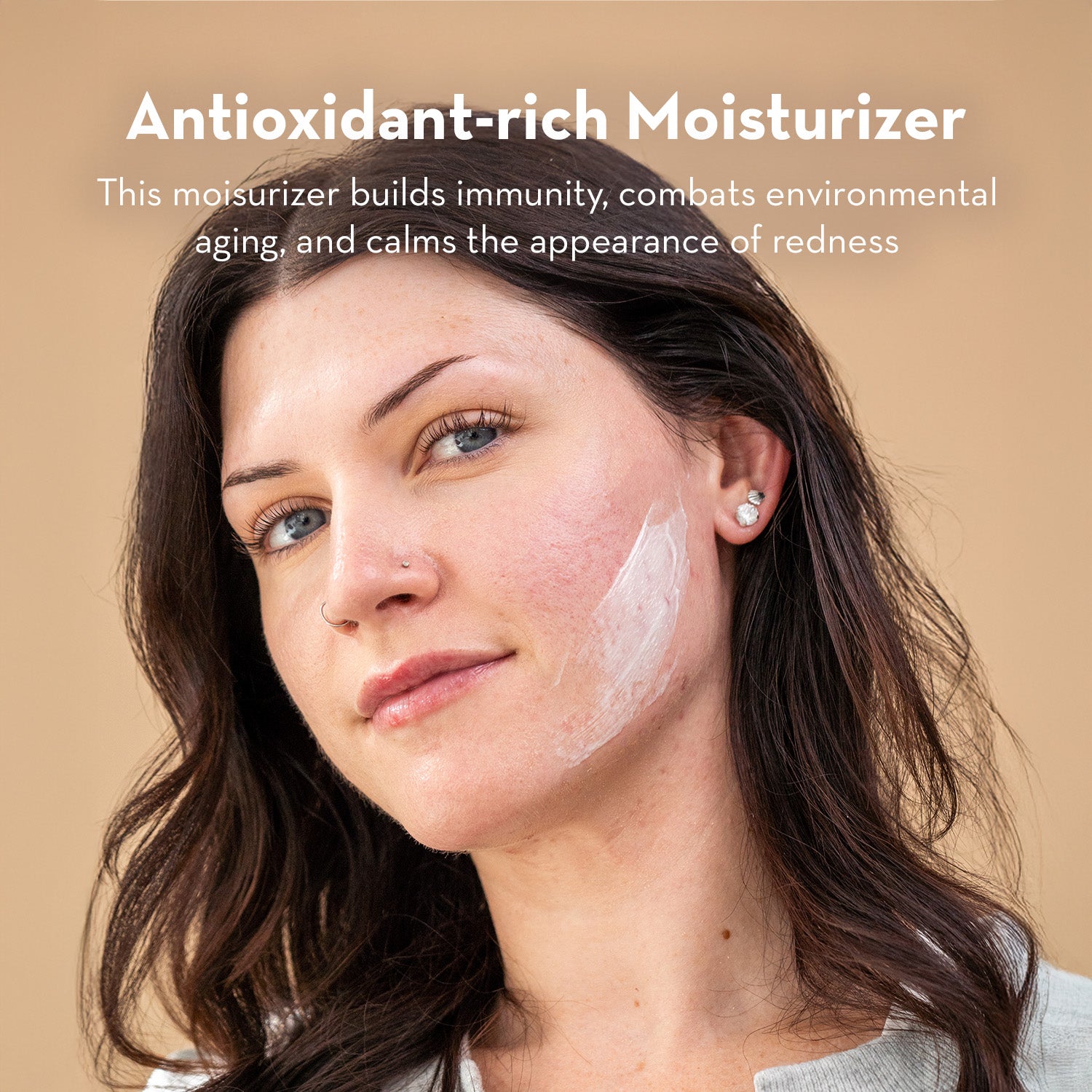 Woman with antioxidant-rich moisturizer on her face against a beige background