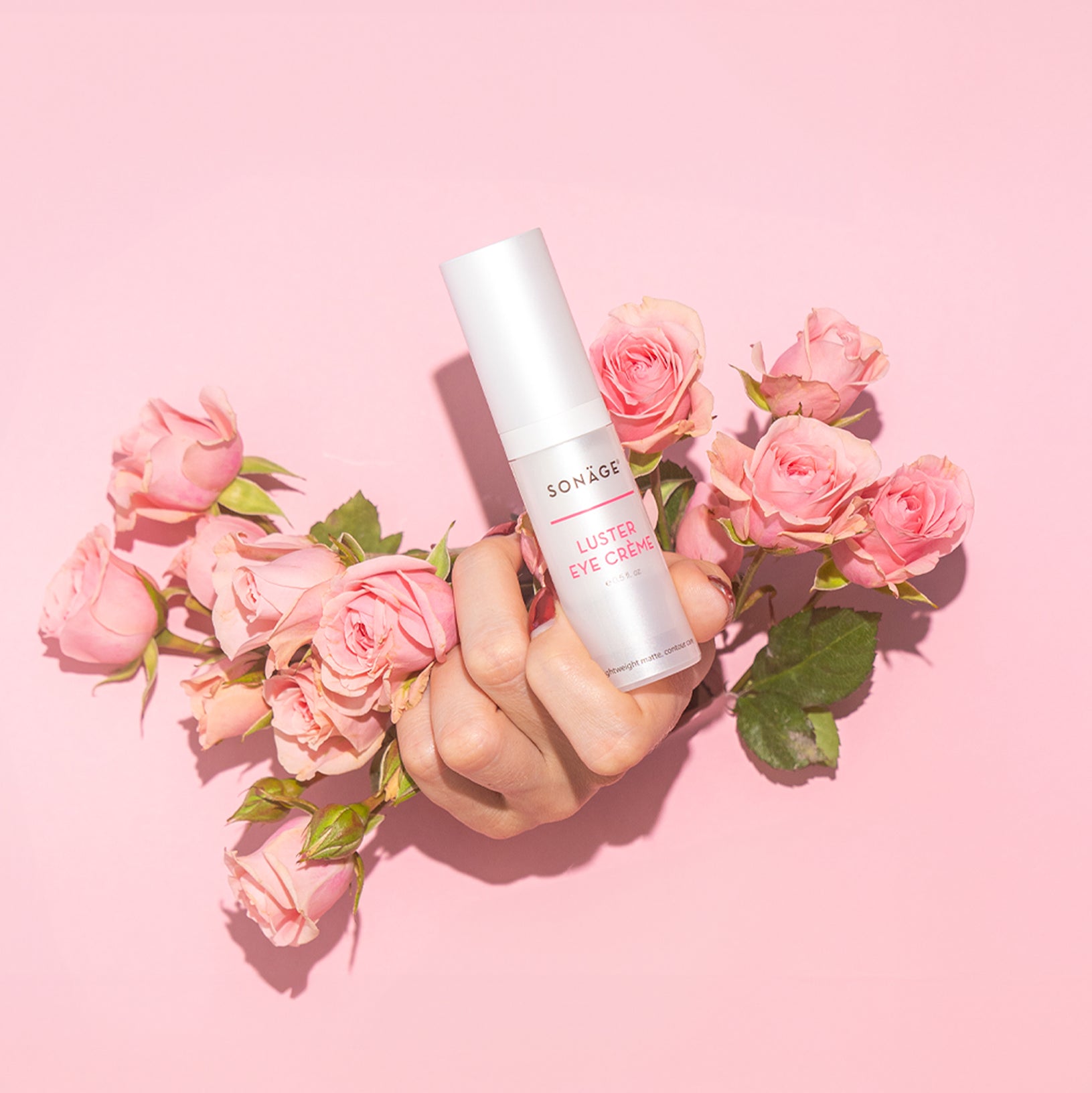 Luster Eye cream being held up in the hands with some flowers and roses around