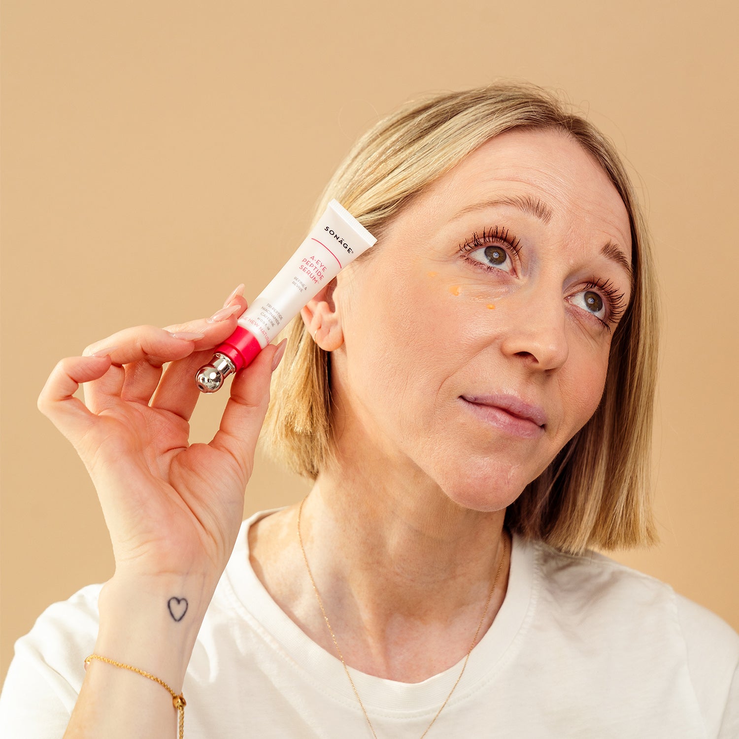 model holding a eye serum with droplet of serum under eyes