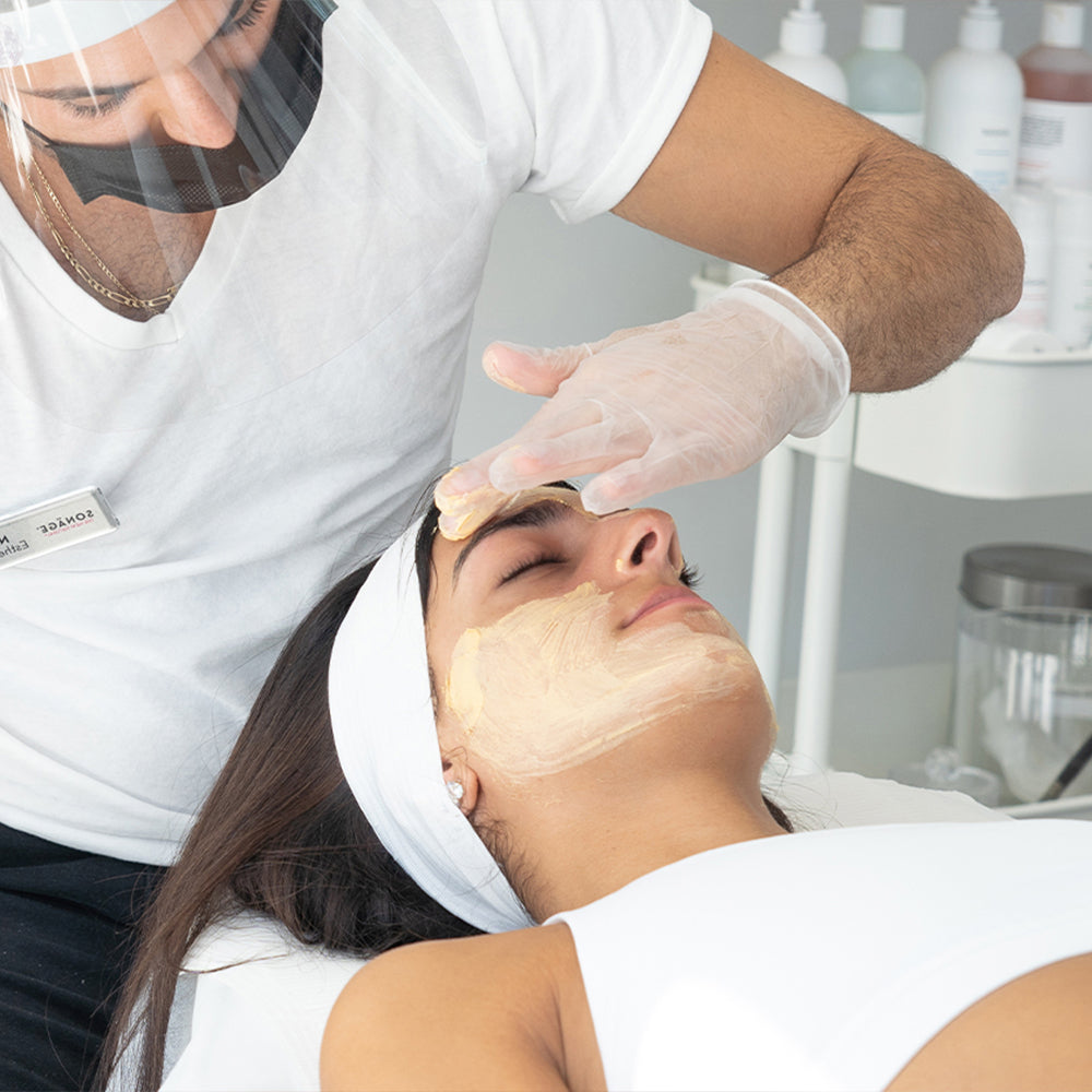 Person applying a facial mask to another person in a clinical setting.